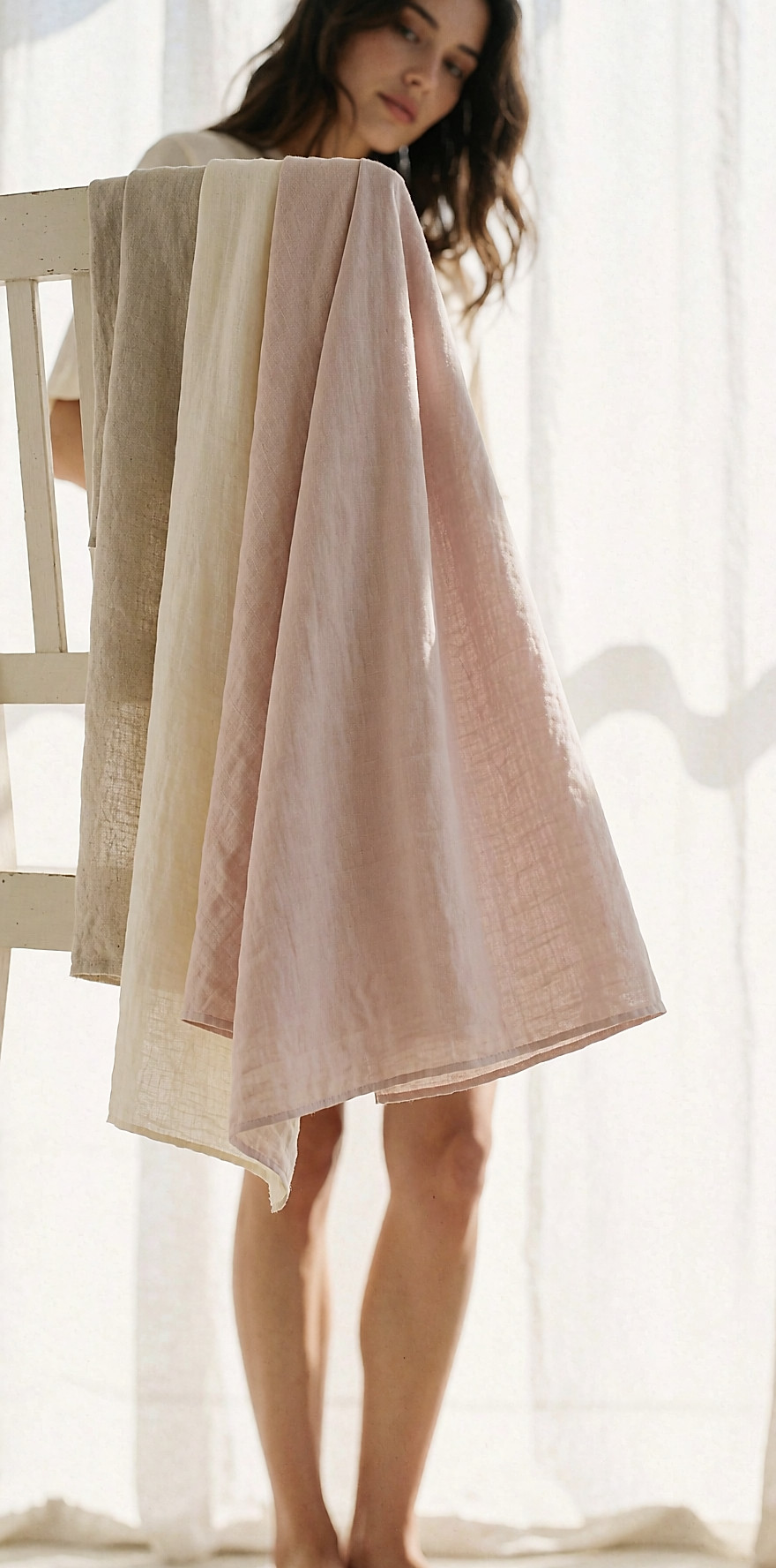 Three summer fabrics — washed linen, crepe cotton, fluid viscose — draped over the back of a pale wood chair