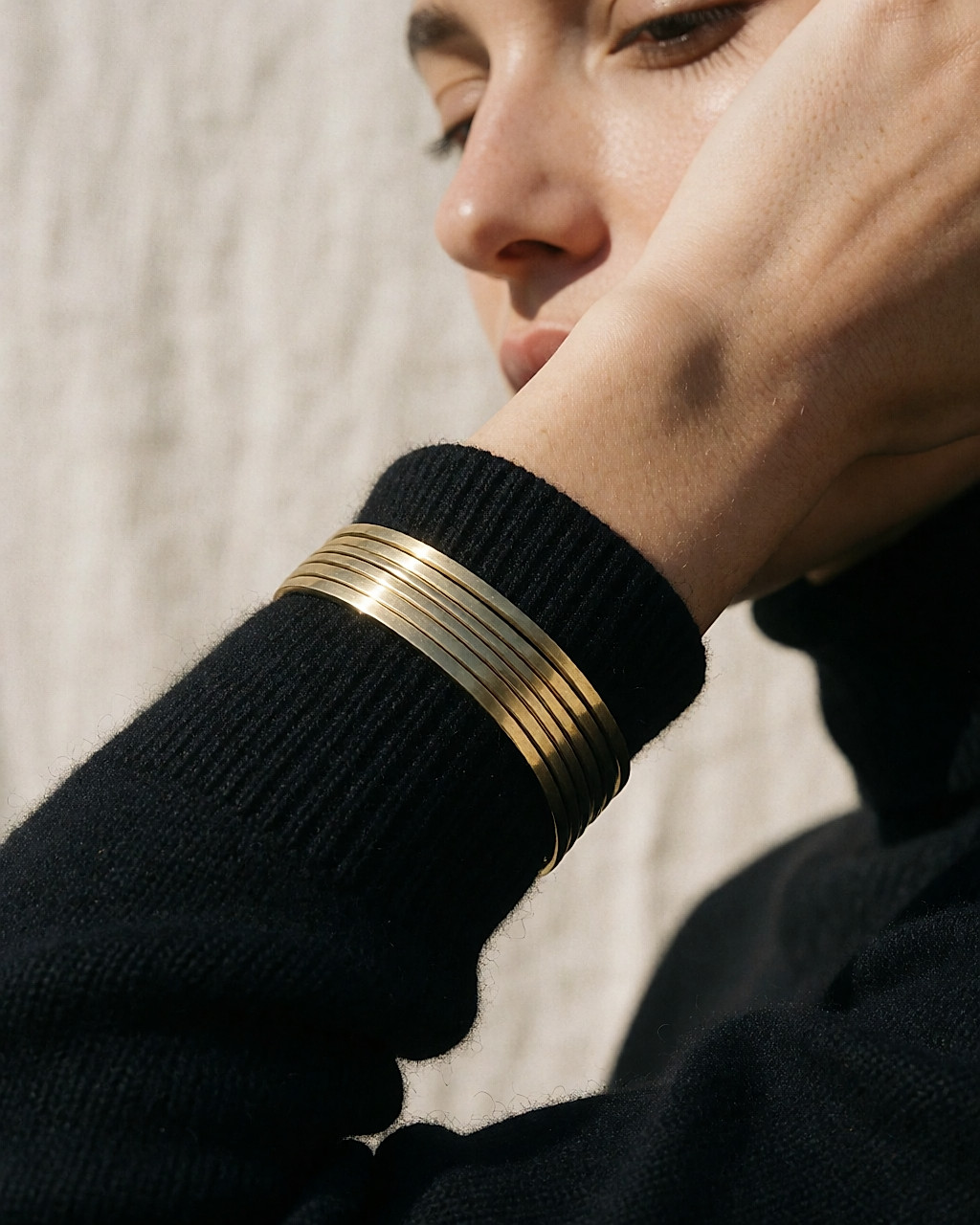 Poignet portant plusieurs bracelets fins en laiton recyclé sur une manche en maille noire