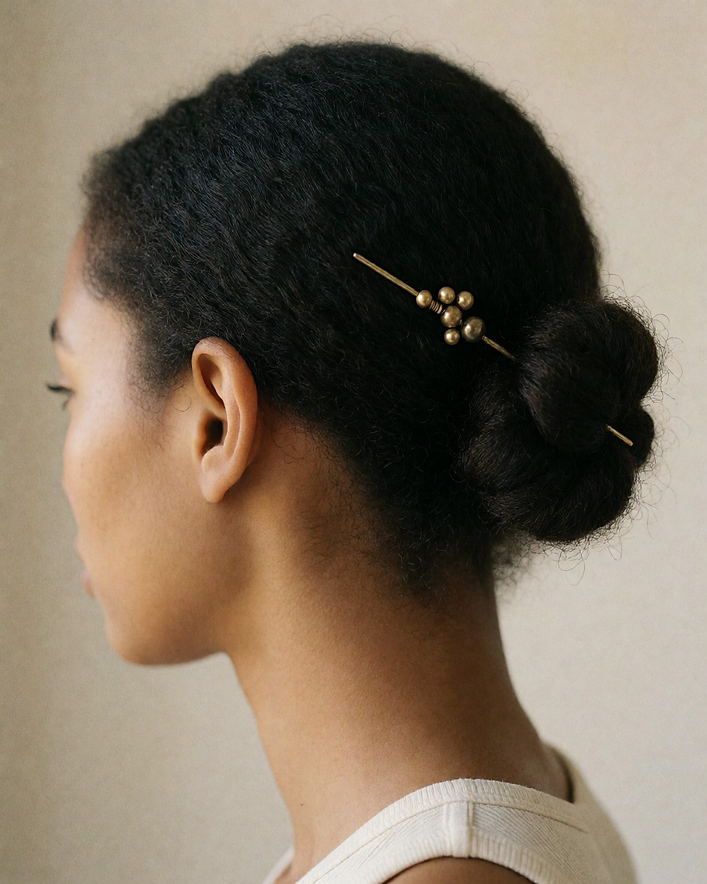 Épingle à cheveux dorée glissée dans un chignon bas, vue de trois quarts arrière
