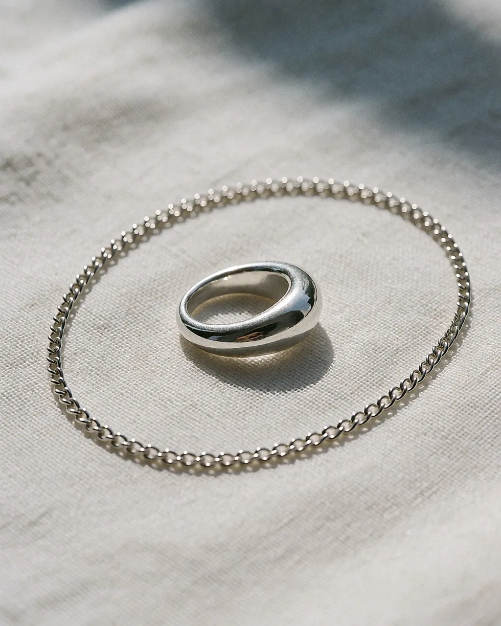 Skulpturaler Ring und feine Kette aus 925er Recycling-Silber auf rohem Leinen