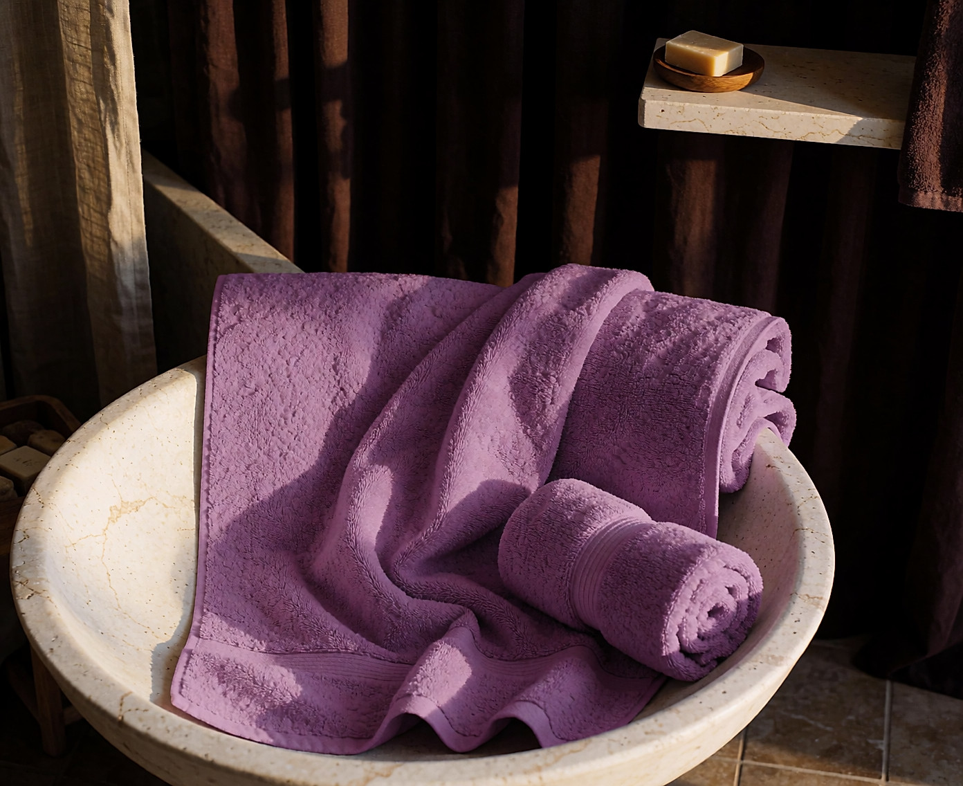 Grand drap de bain éponge couleur sable plié sur un banc de pierre, serviette roulée à côté