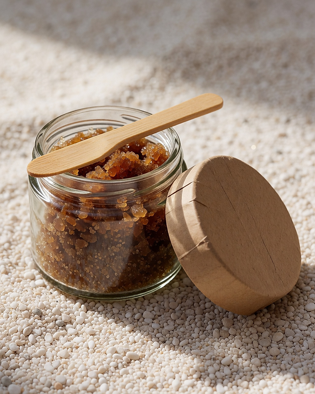 Pot de verre ouvert de gommage au sucre, grains visibles et spatule en bois posée sur le bord