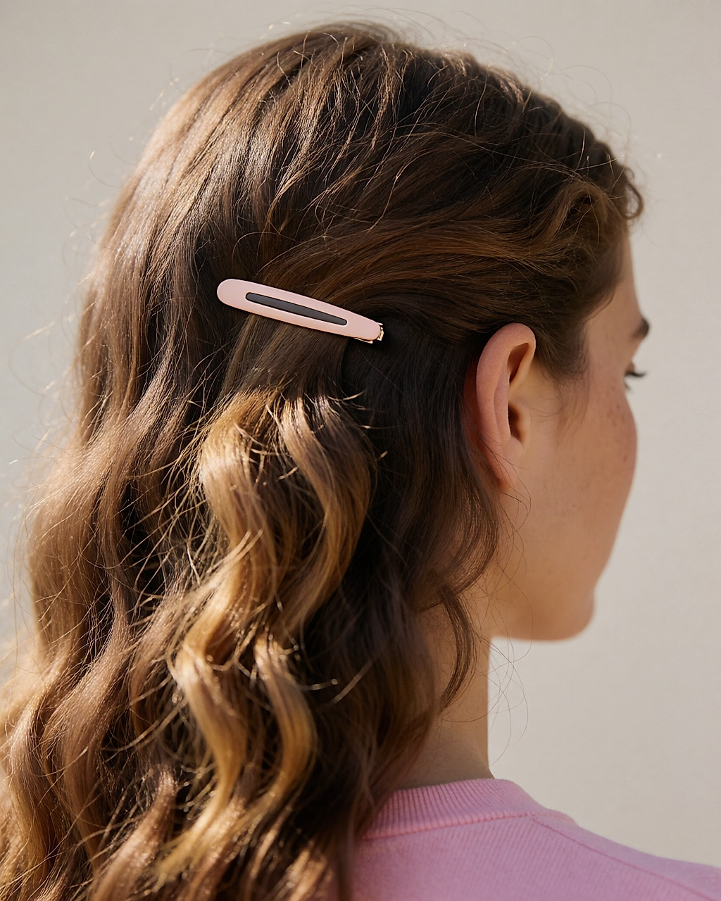 Barrette dorée rosée fixant une mèche ondulée derrière l'oreille, gros plan