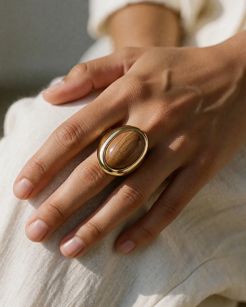 Nahaufnahme eines goldenen Rings mit holzartigem Cabochon an einer Hand auf hellem Leinen