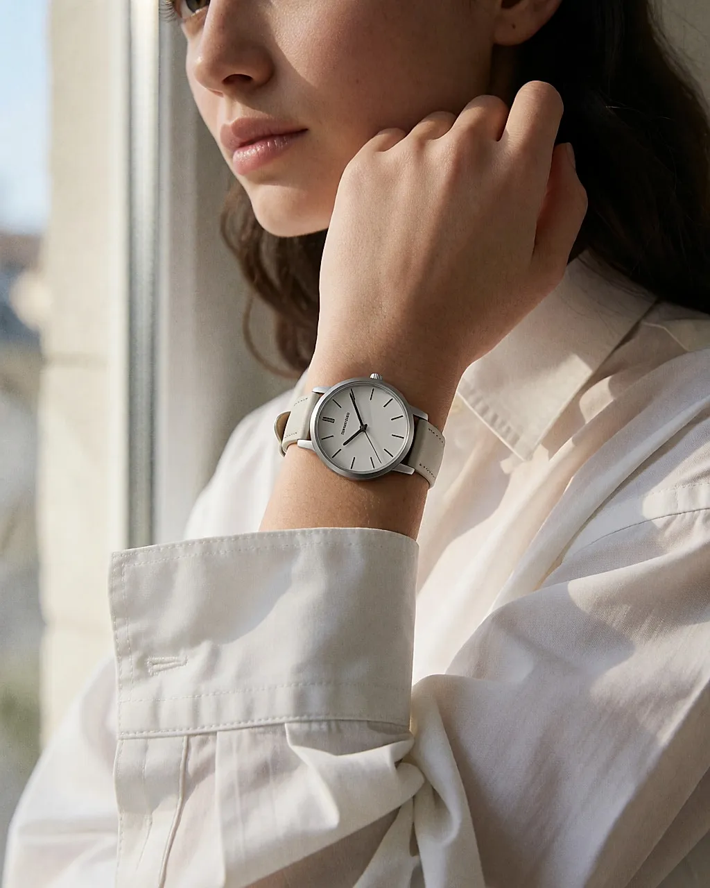Feine Uhr mit Edelstahlgehäuse und hellem Lederband am Handgelenk, Hemdsärmel hochgeschoben