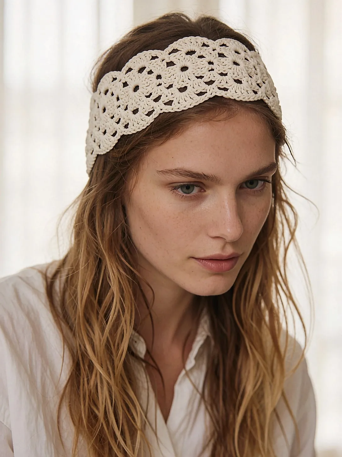 Breites Häkel-Haarband in Creme, das leicht gewellte Haare hält, von schräg hinten gesehen