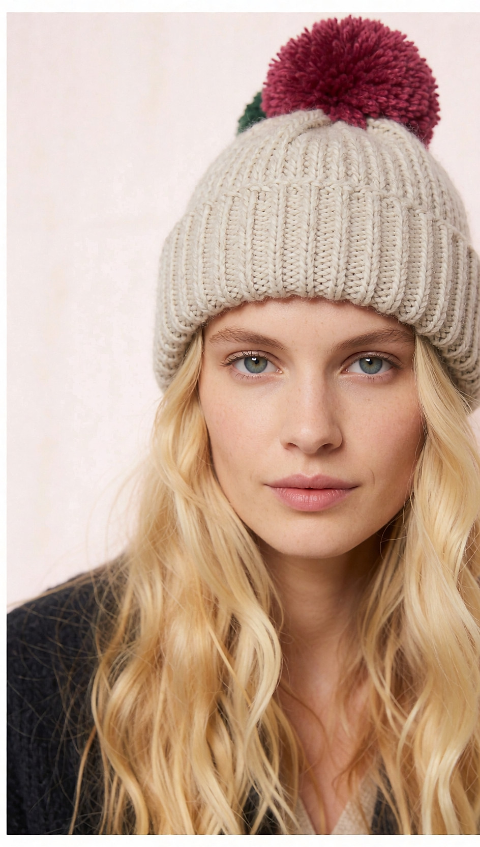 Trois bonnets en maille à pompon avoine, framboise et vert posés sur un linge clair