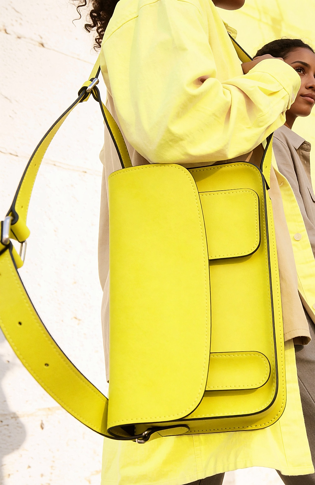 Jeune femme de dos portant un cartable jaune fluo en bandoulière sur une tenue beige, rue claire