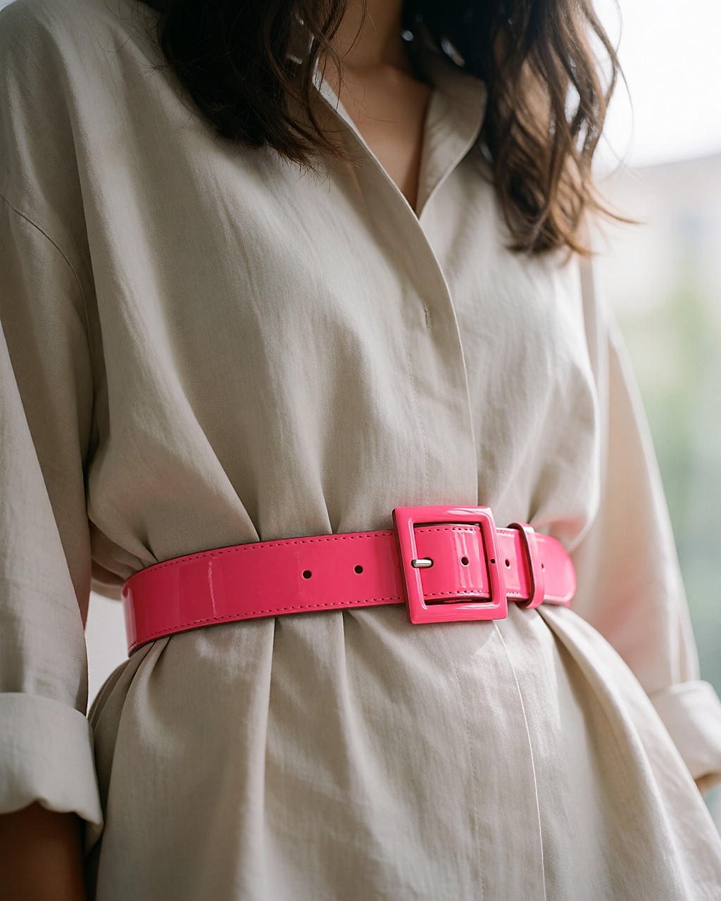 Ceinture en cuir vernis rose fluo serrant une blouse neutre