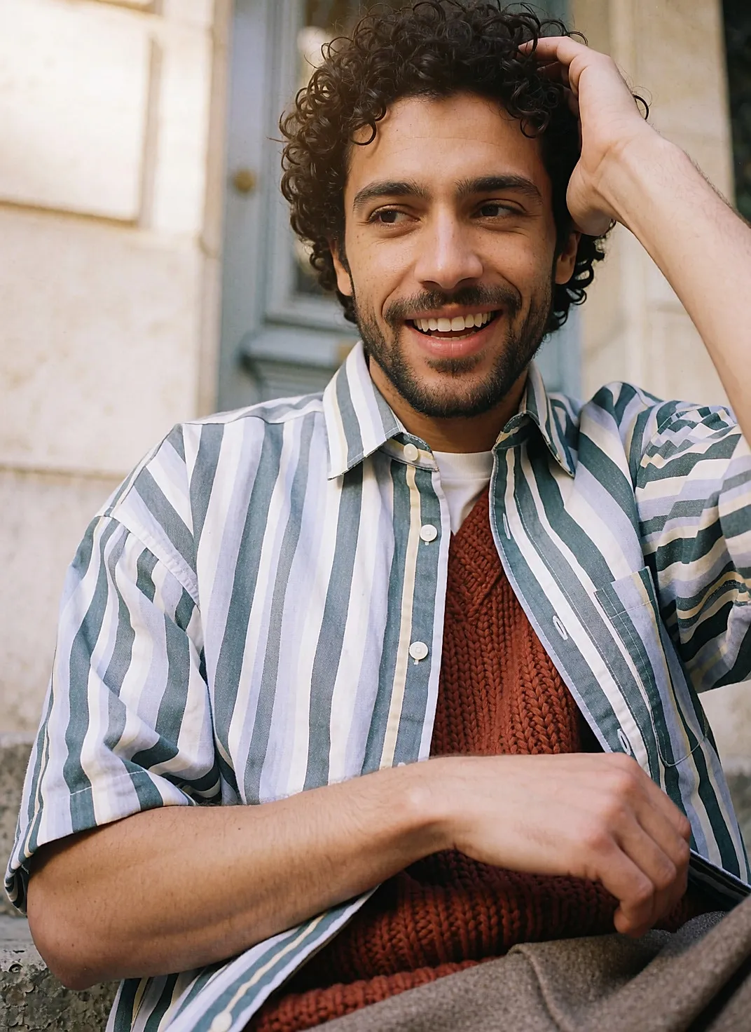 Hombre con punto grueso color óxido llevado ancho, camisa abierta sobre camiseta, sentado en unos escalones