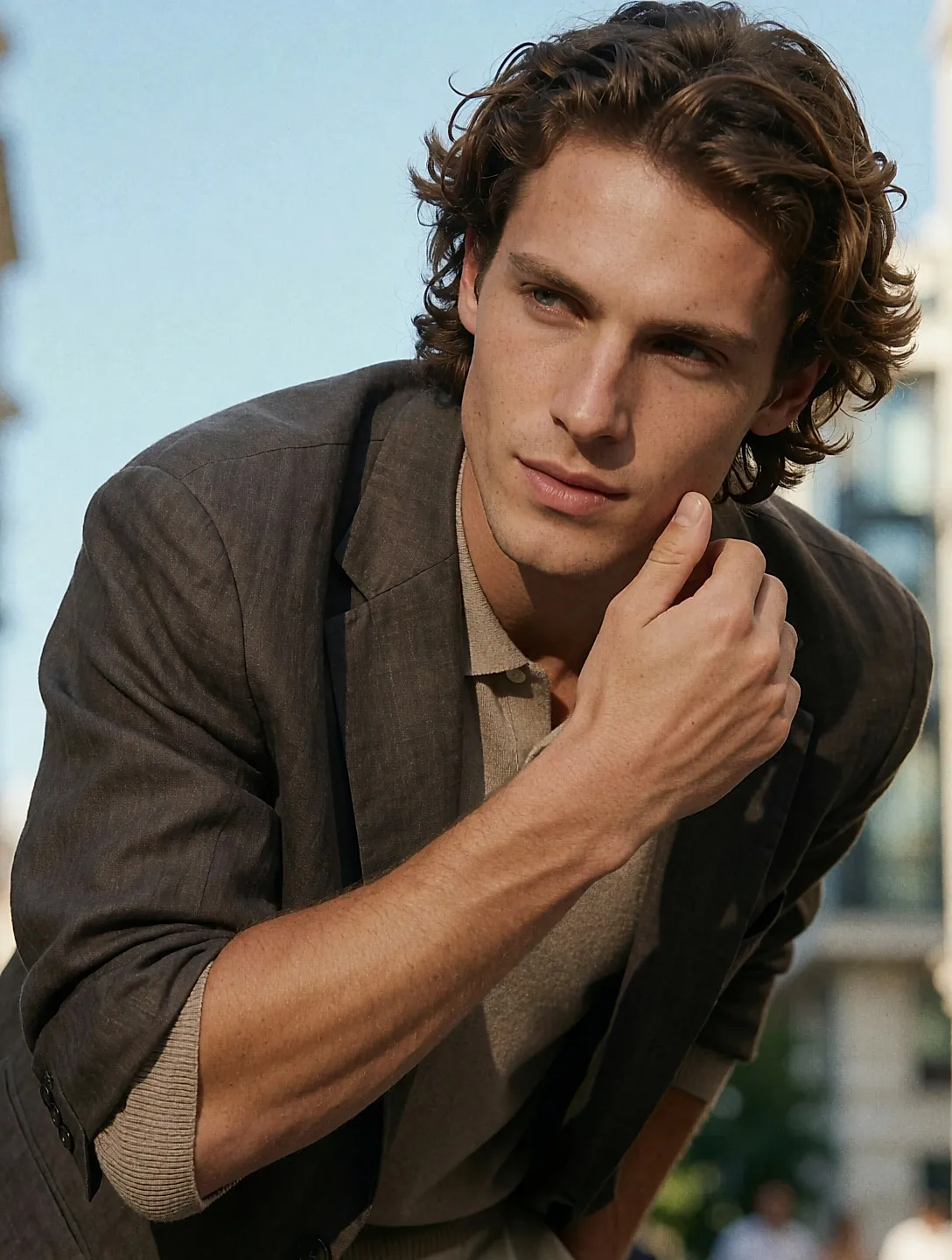 Hombre con short corto beige combinado con punto fino y blazer de lino, calle urbana soleada