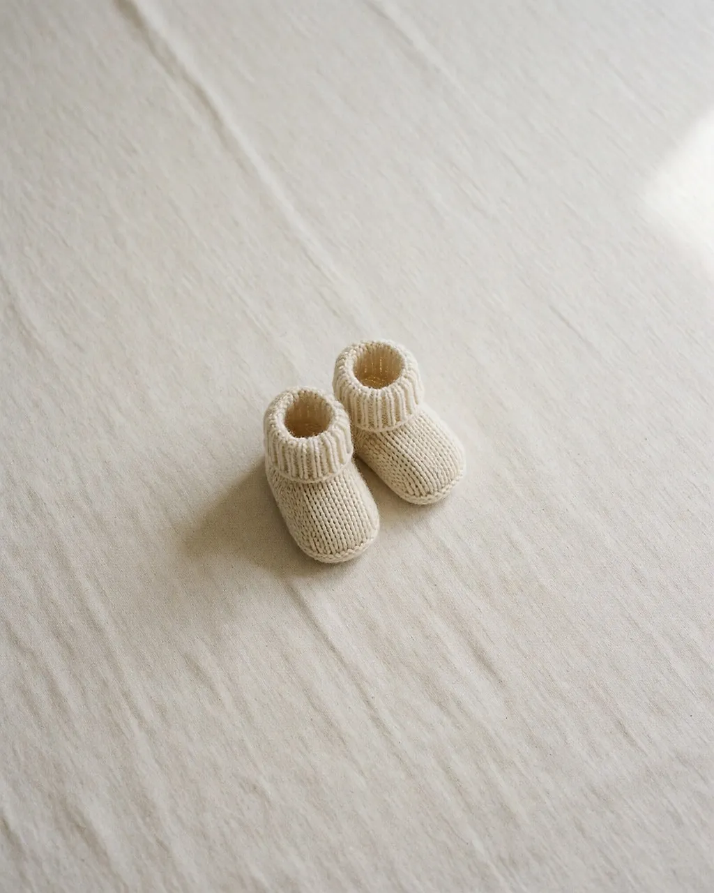 Ein Paar gestrickte Babyschühchen, allein auf einem weißen Leinentuch