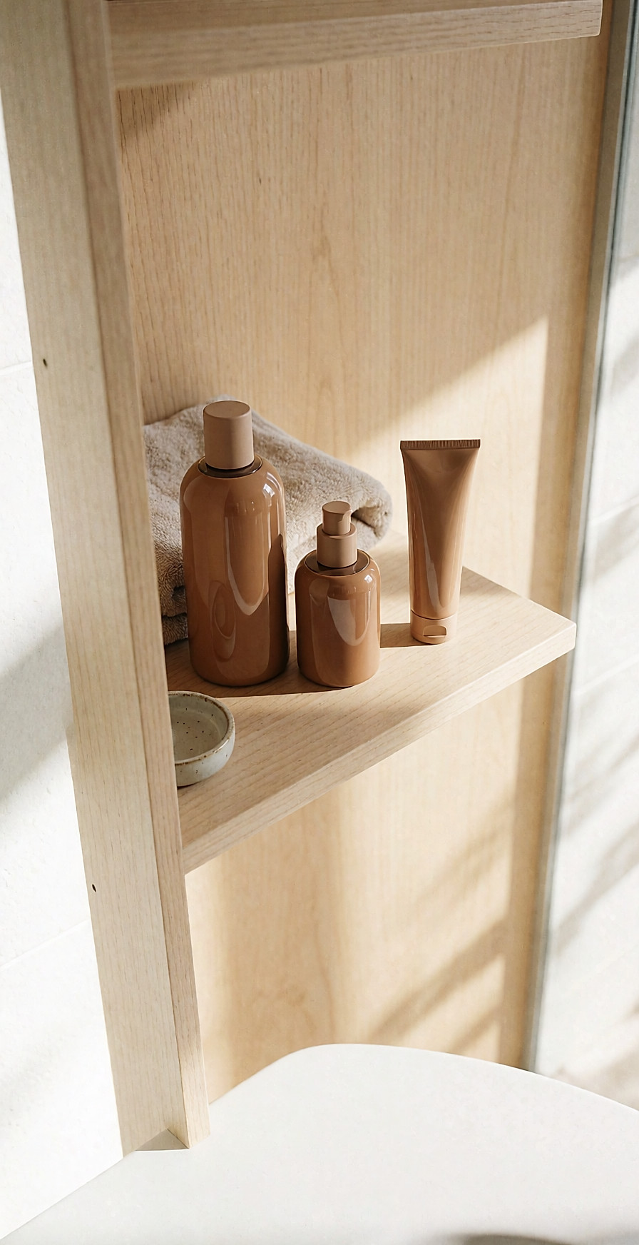 Three self-tan containers in different sizes lined up on a light wooden shelf