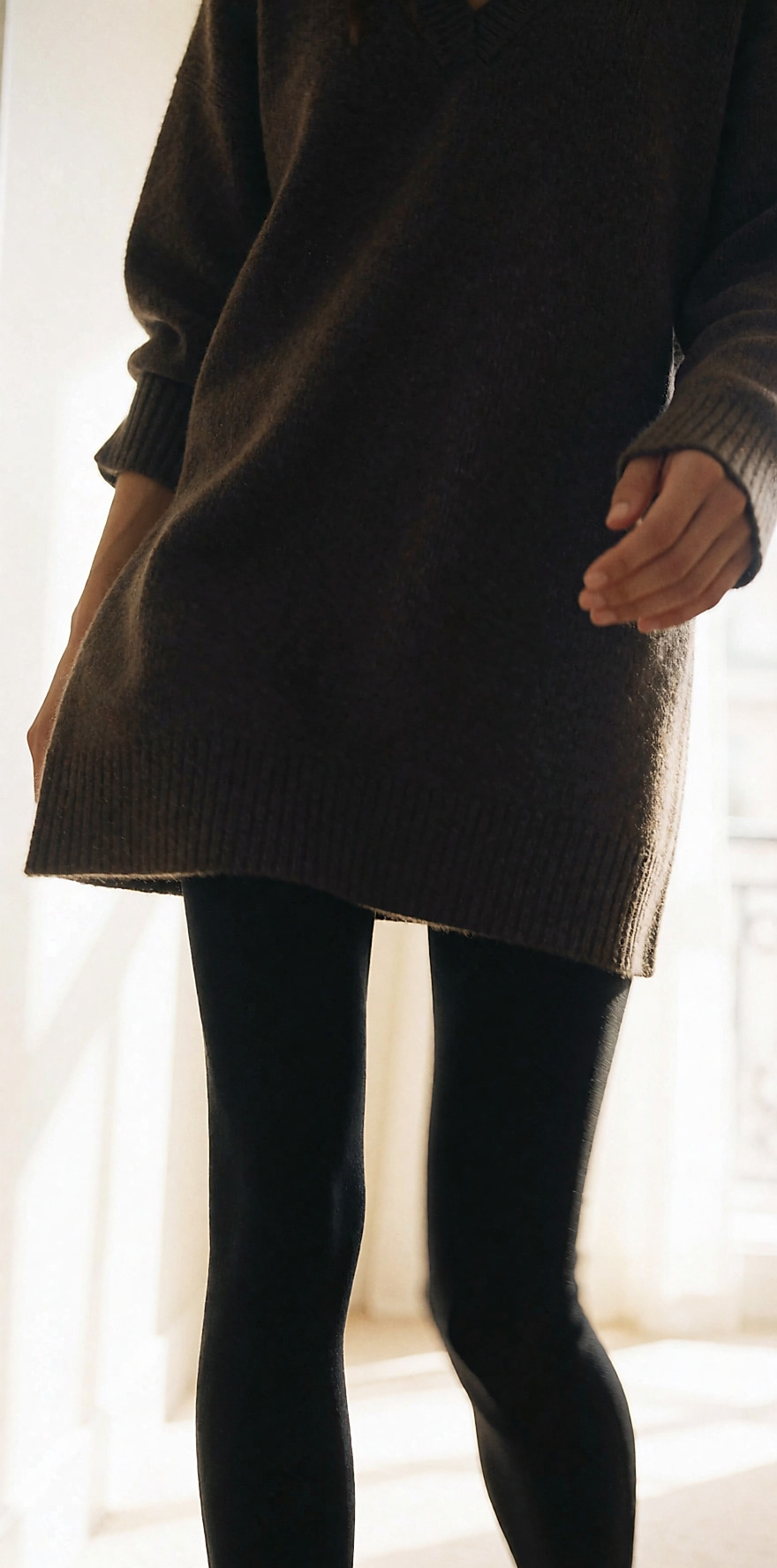 Silhouette en robe pull, leggings noirs et escarpins dans un couloir clair