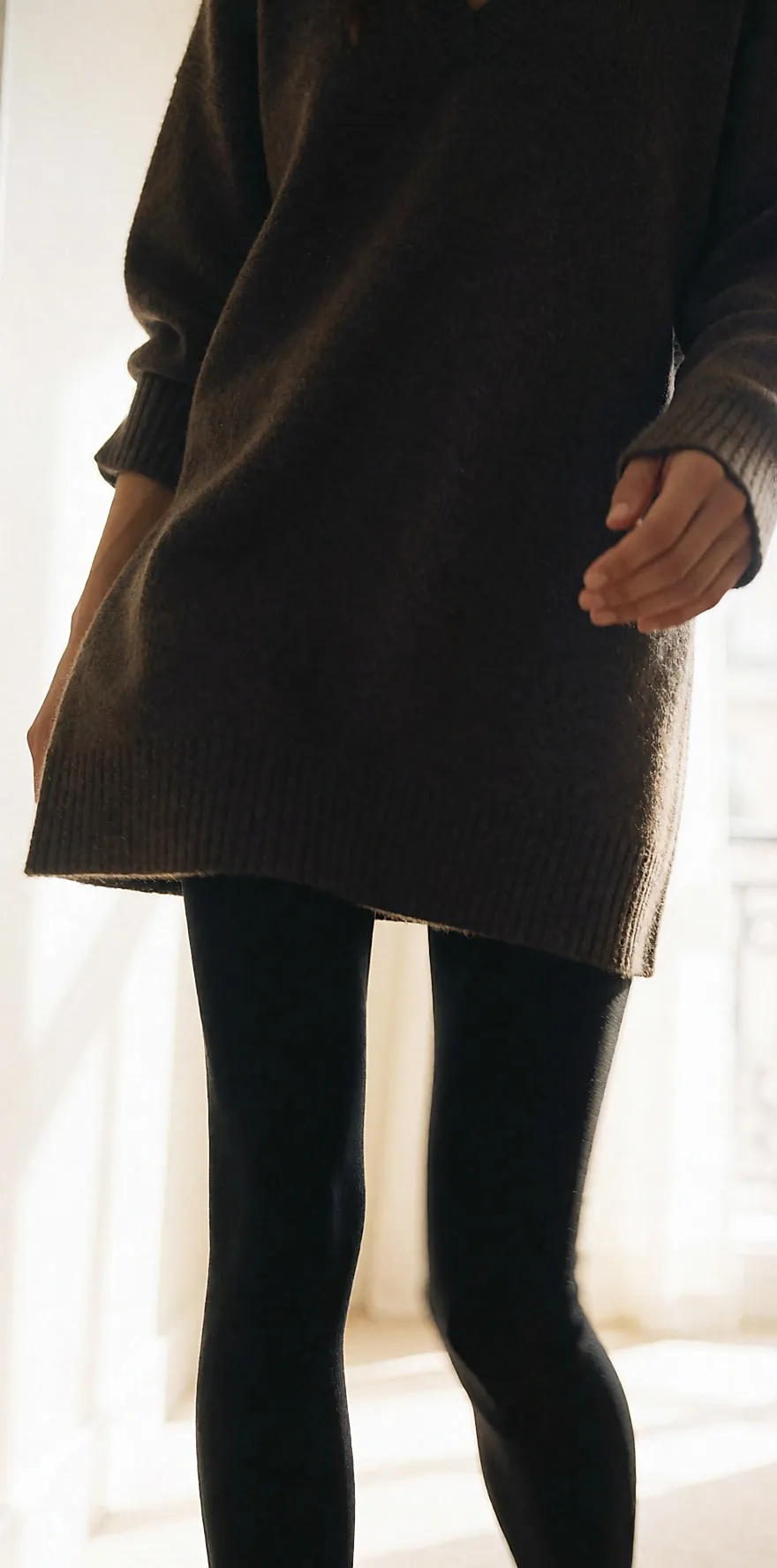 Silueta con vestido de punto, leggings negros y zapatos de salón en un pasillo claro