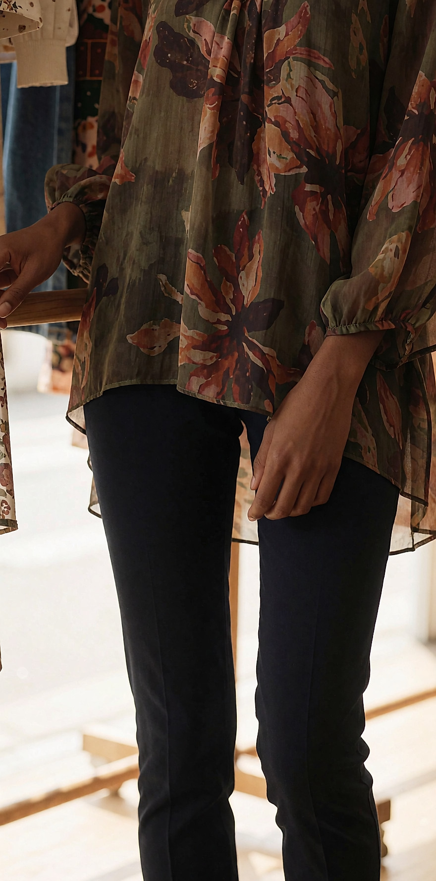 Jeune femme dans une friperie claire, tunique imprimée fluide sur un pantalon slim marine