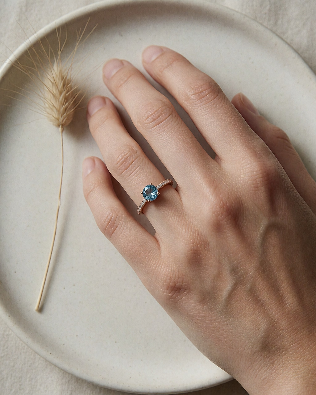 Vue de dessus d'une main portant une bague or rose à topaze bleue et anneau pavé