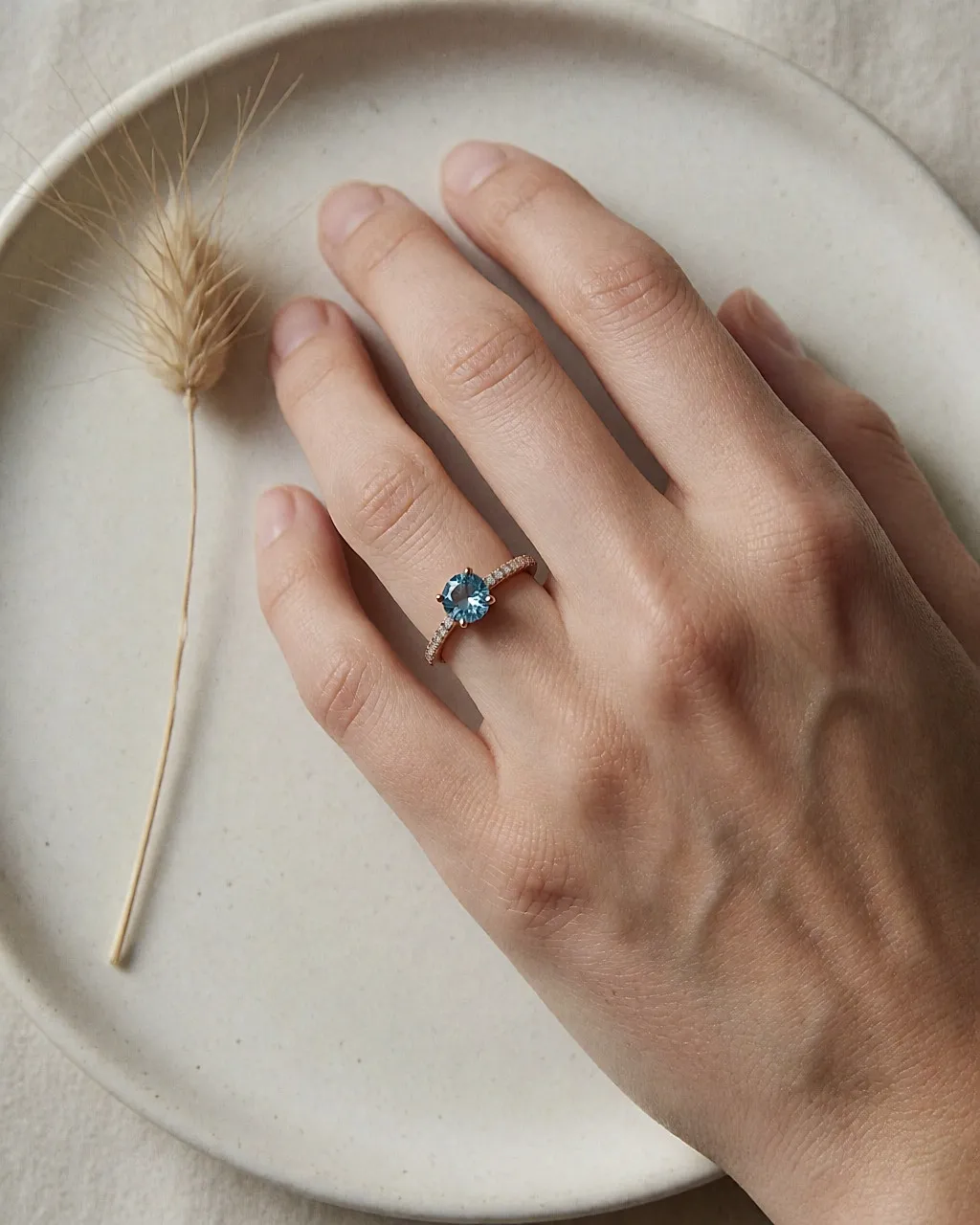 Draufsicht auf eine Hand mit einem Roségoldring mit blauem Topas und pavébesetztem Ringband