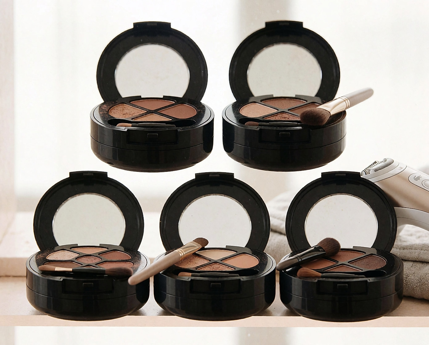 Palette de fards à paupières nude ouverte, pinceau et miroir, épilateur flou au second plan