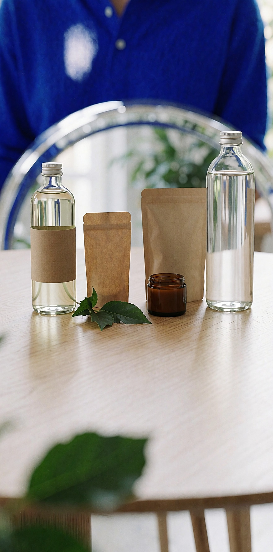 Eau florale en verre, recharge en kraft et pots en verre alignés sur une table en chêne clair