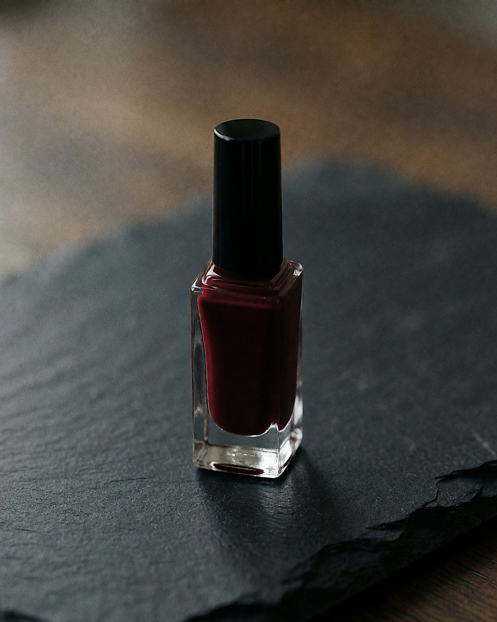 Flacon de vernis bordeaux profond sur une surface d'ardoise sombre