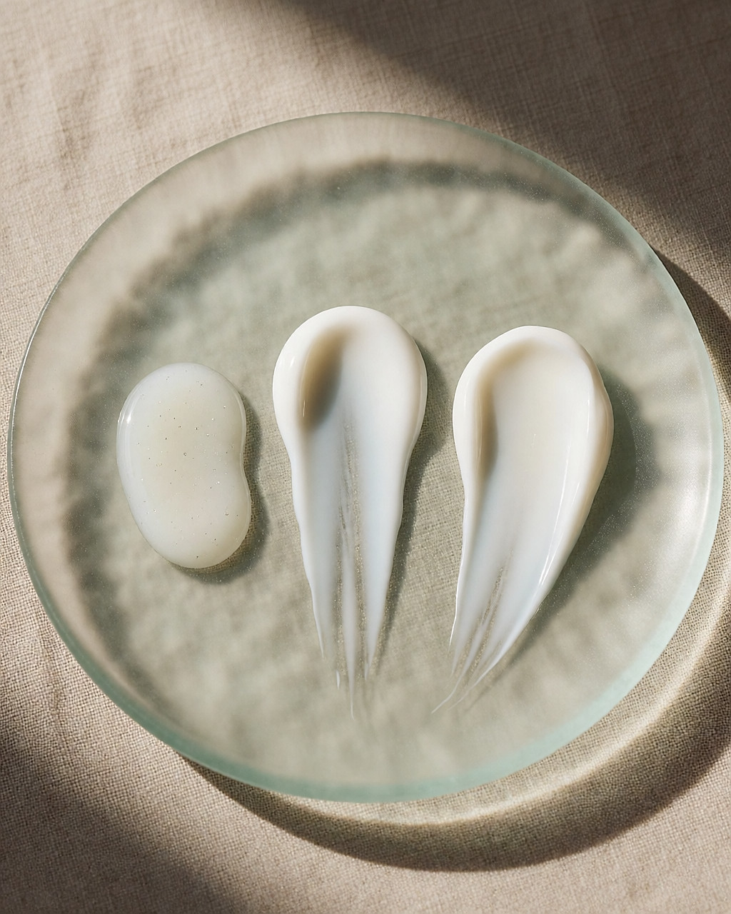 Trois textures de soin alignées, du sérum fluide à la crème épaisse, sur une plaque de verre