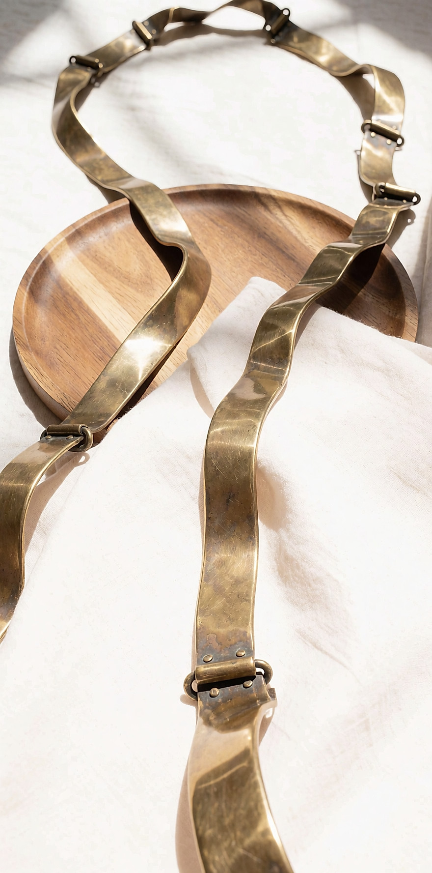 Long necklace in solid brass with a warm patina, laid on light linen