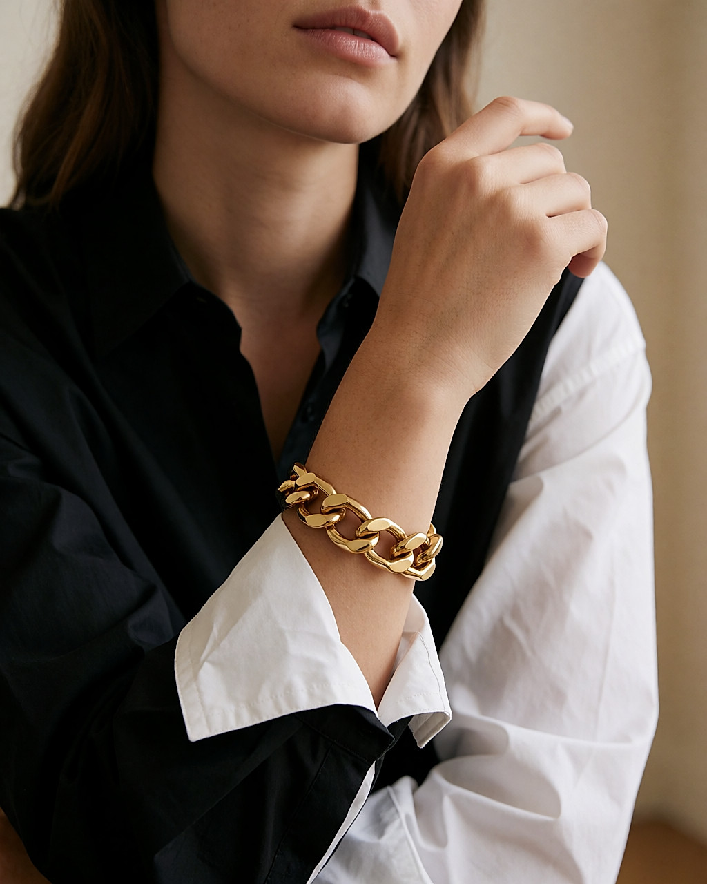 Wrist wearing a gold-tone chunky chain bracelet over the sleeve of a poplin shirt