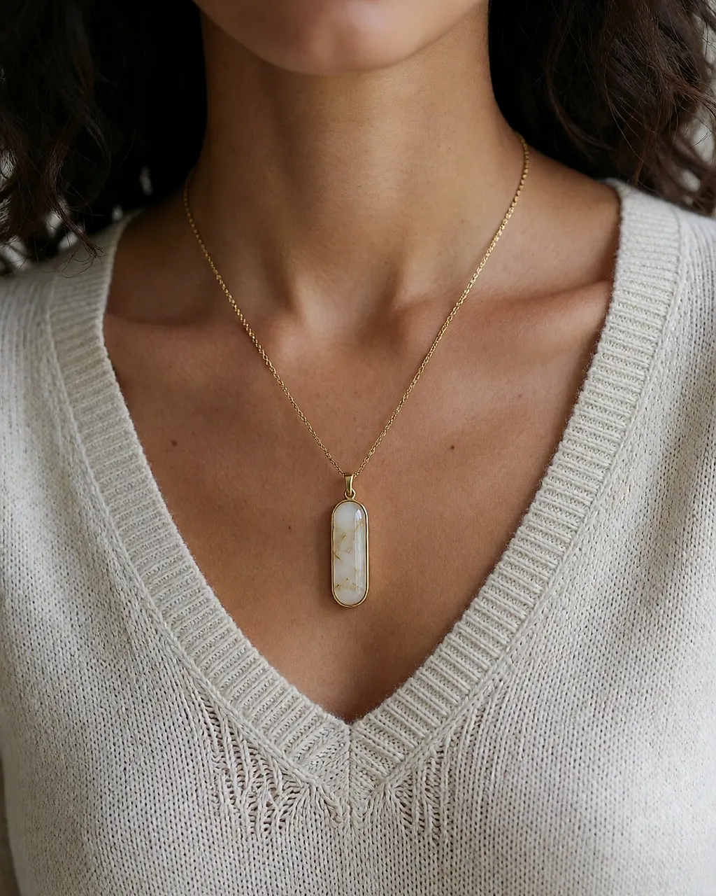Pendentif long à cabochon opalin dans le creux d'un col V, sur une maille claire