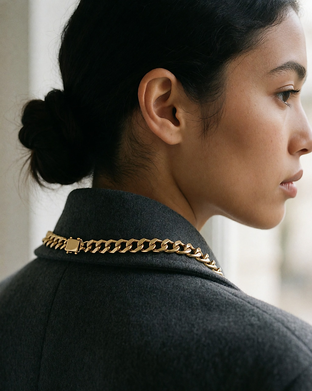 Clasp of a worn gold-tone necklace, seen at the nape of a young woman with a low bun