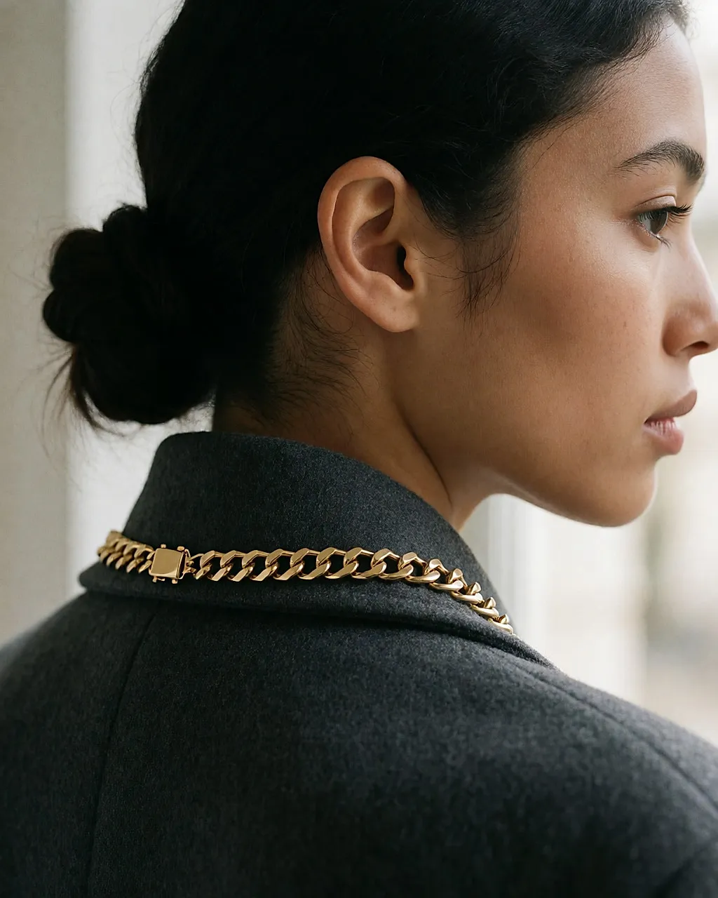 Fermoir d'un collier doré usé, vu dans la nuque d'une jeune femme au chignon bas