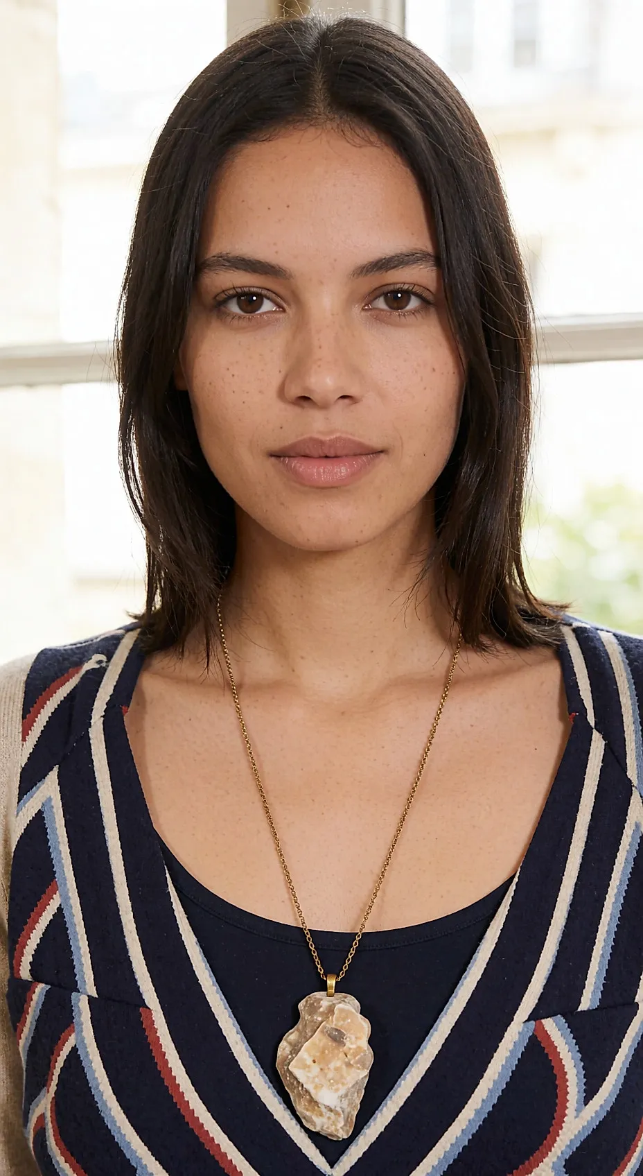 Young woman wearing a long necklace with a raw stone pendant over a plain oat-coloured knit
