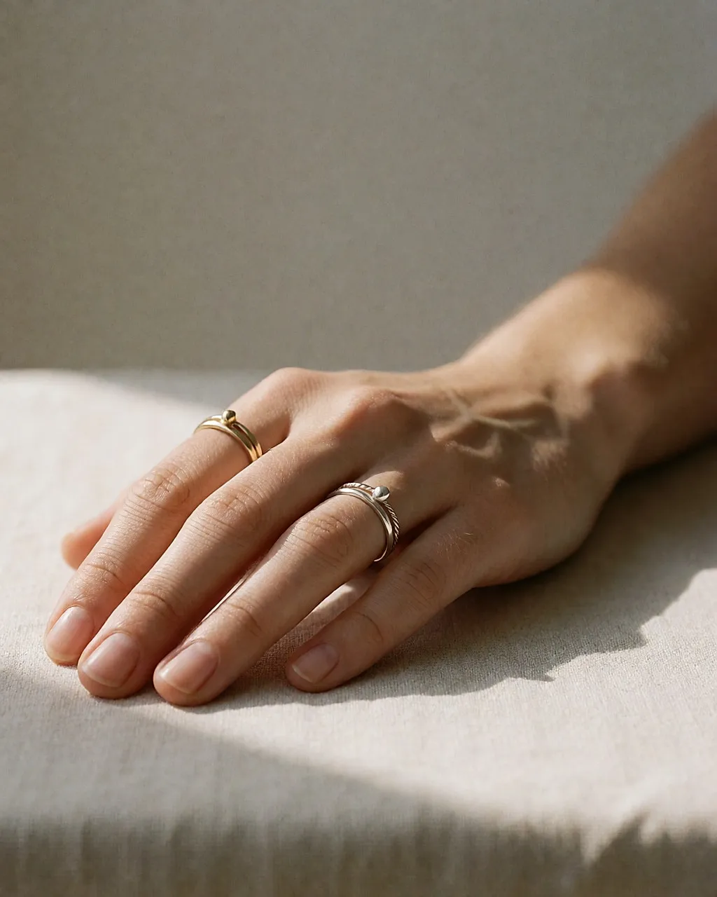 Hand resting on pale linen, three fine rings in gold, silver and raw stone