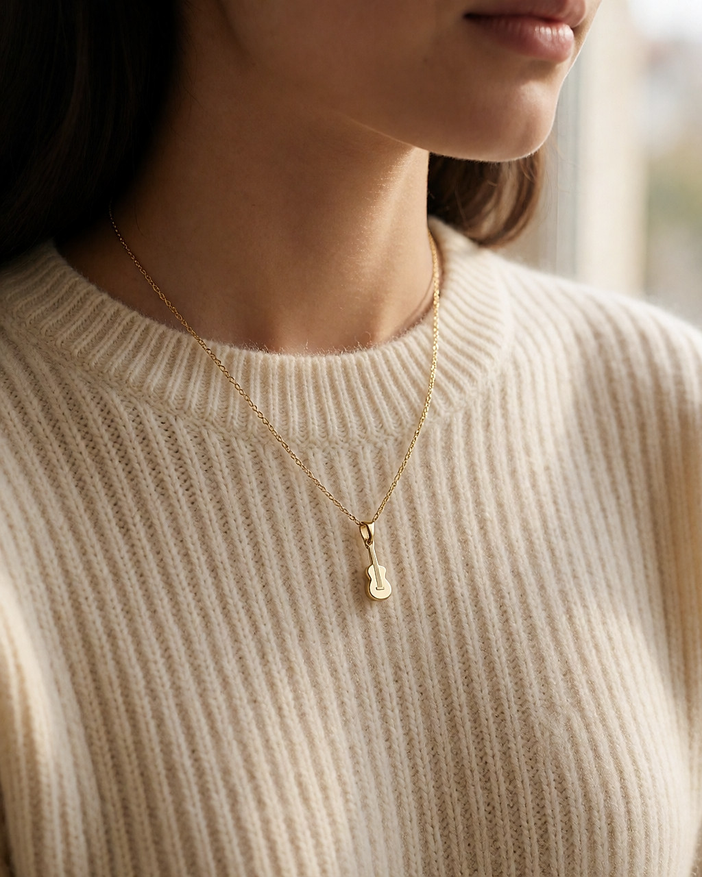 Pendentif guitare doré sur une chaîne fine, porté sur un pull crème côtelé
