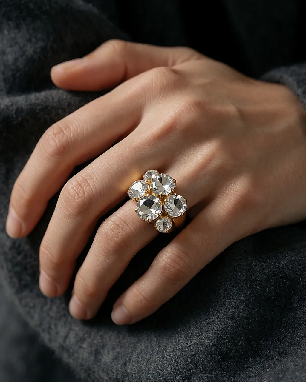 Goldener Statement-Ring mit facettierten Kristallen, an einer Hand auf grauer Wolle
