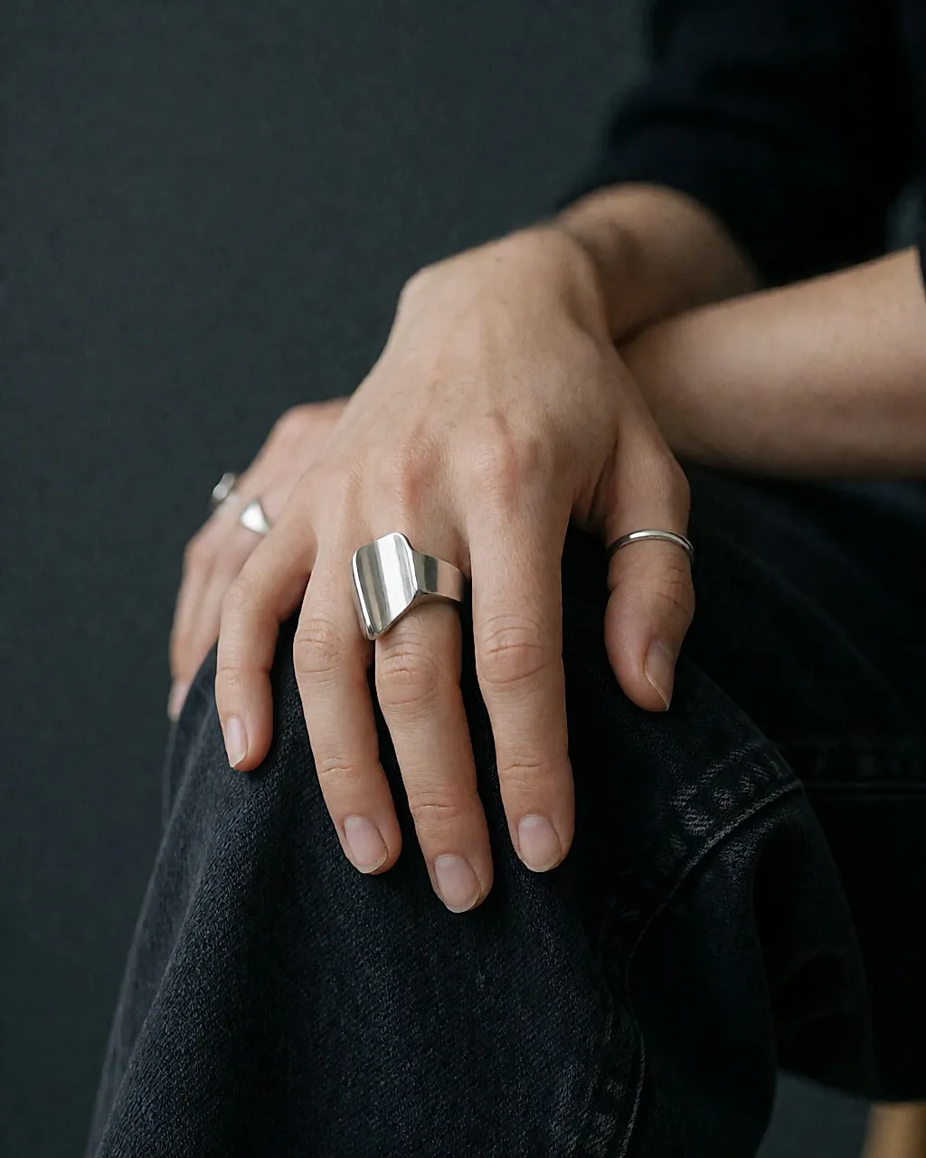 Eine Hand auf dunkler Rohjeans, geschmückt mit einem einzigen Statement-Ring aus gebürstetem Edelstahl mit skulpturalem Volumen