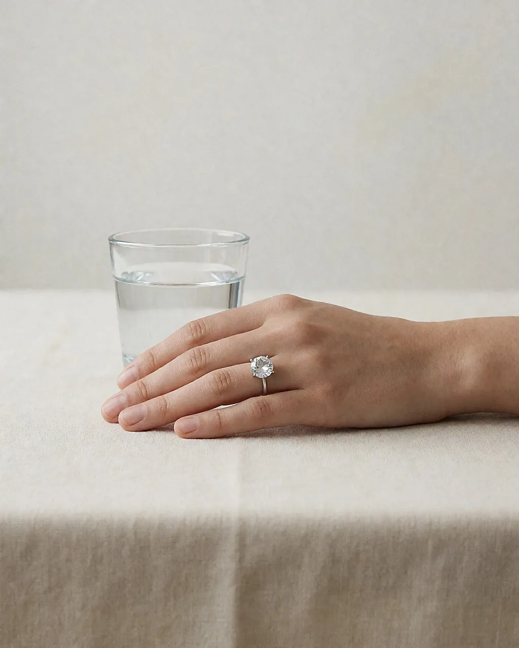 Ein Ring mit großem facettiertem Kristall an einer Hand auf cremefarbenem Leinentuch, Tageslicht