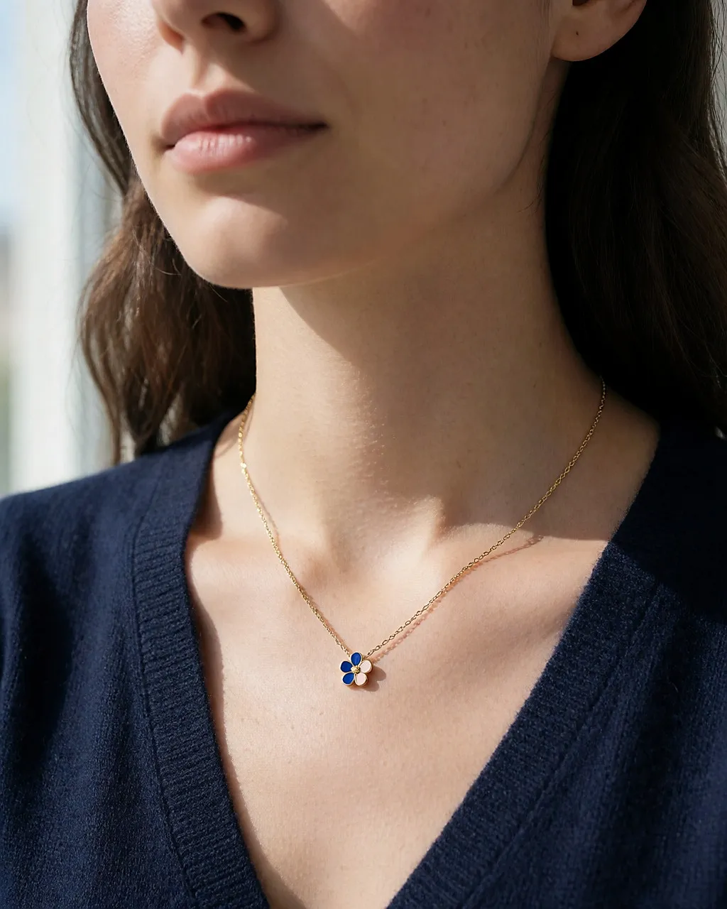 Feine goldene Kette mit blau-rosa emailliertem Blumenanhänger auf marineblauem Strick
