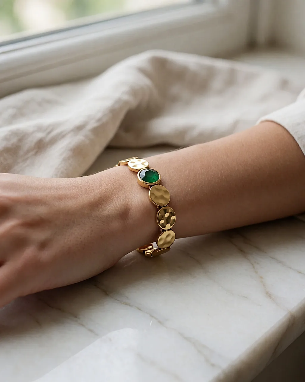 Goldenes Armband mit gehämmerten Gliedern und grünem Stein am Handgelenk auf Marmor