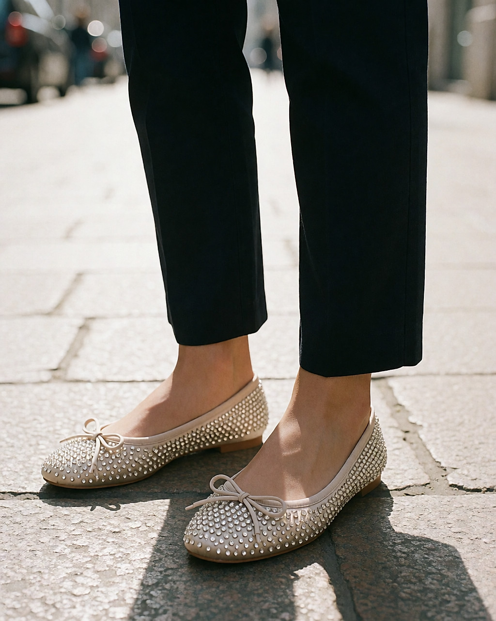 Ballerines de satin beige poudré ornées de cristaux, portées sur un pavé milanais