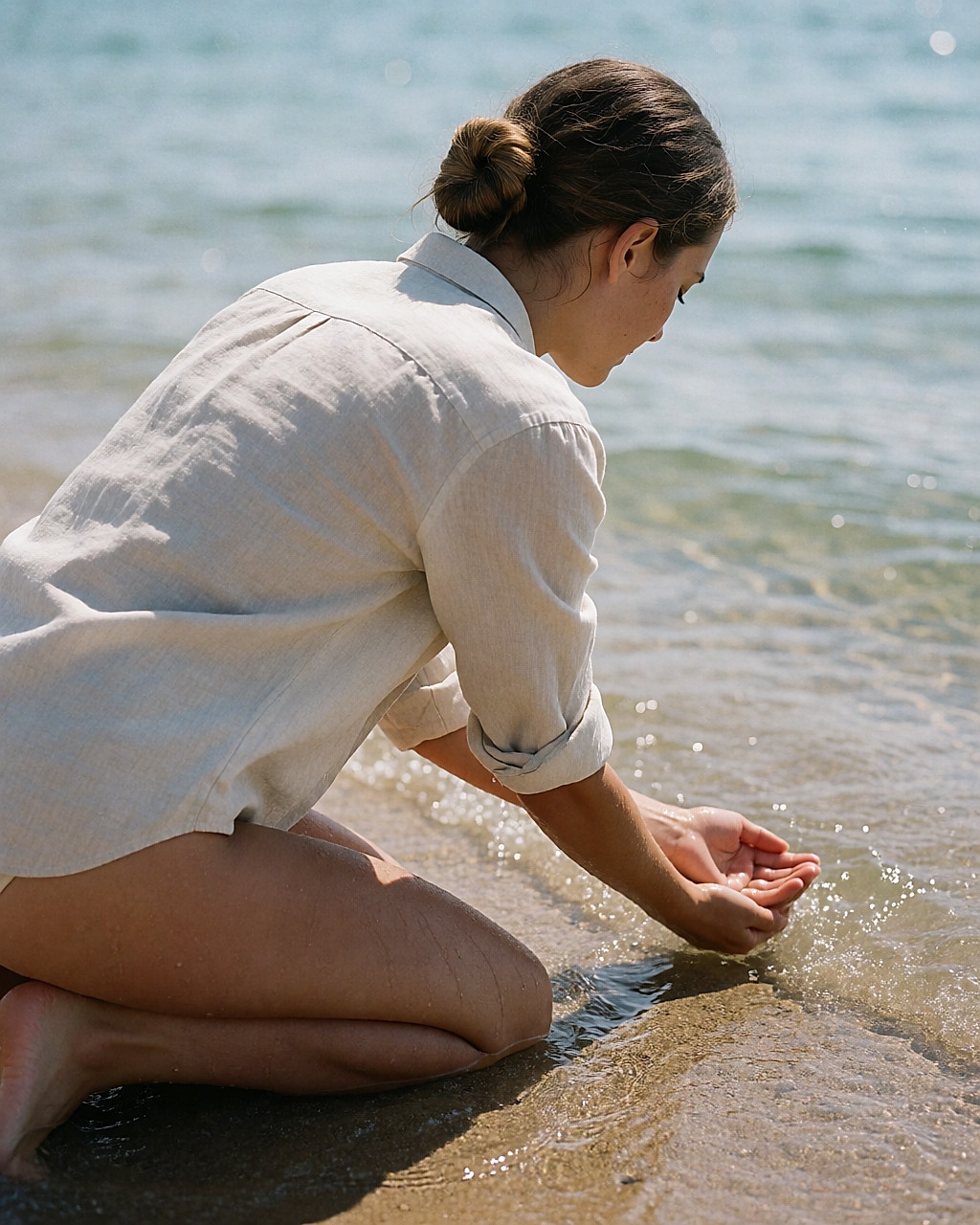 Une femme agenouillée au bord de la mer rince son avant-bras à l'eau salée