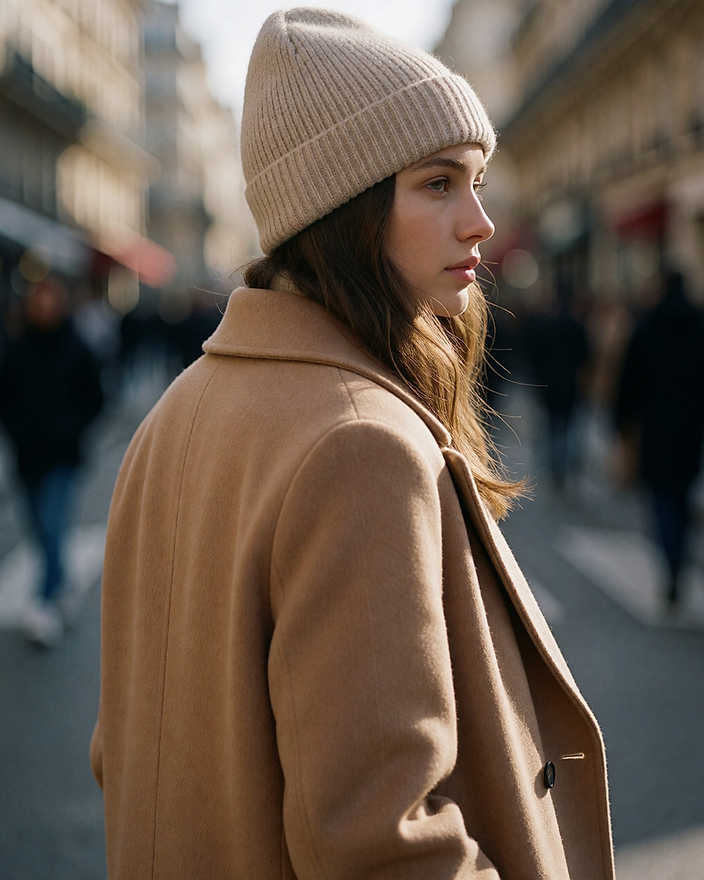 Jeune femme de dos dans la rue en hiver, bonnet côtelé beige et manteau de laine camel