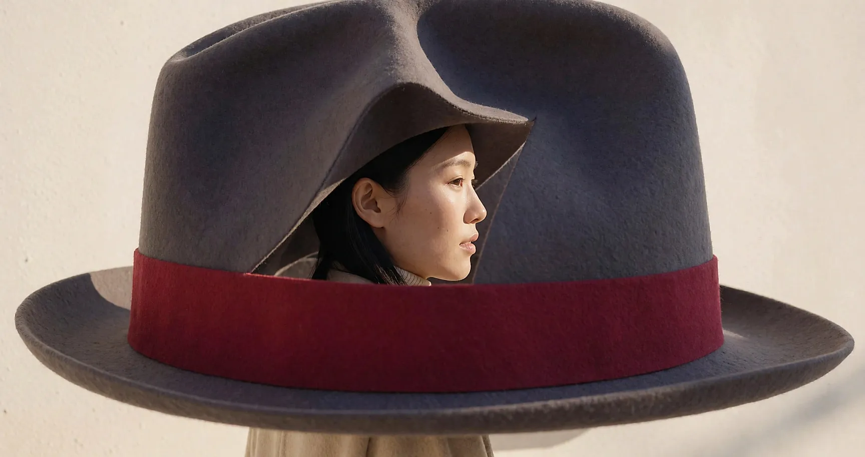 Profil d'une jeune femme coiffée d'un chapeau de feutre sculpté au bord asymétrique, fond neutre