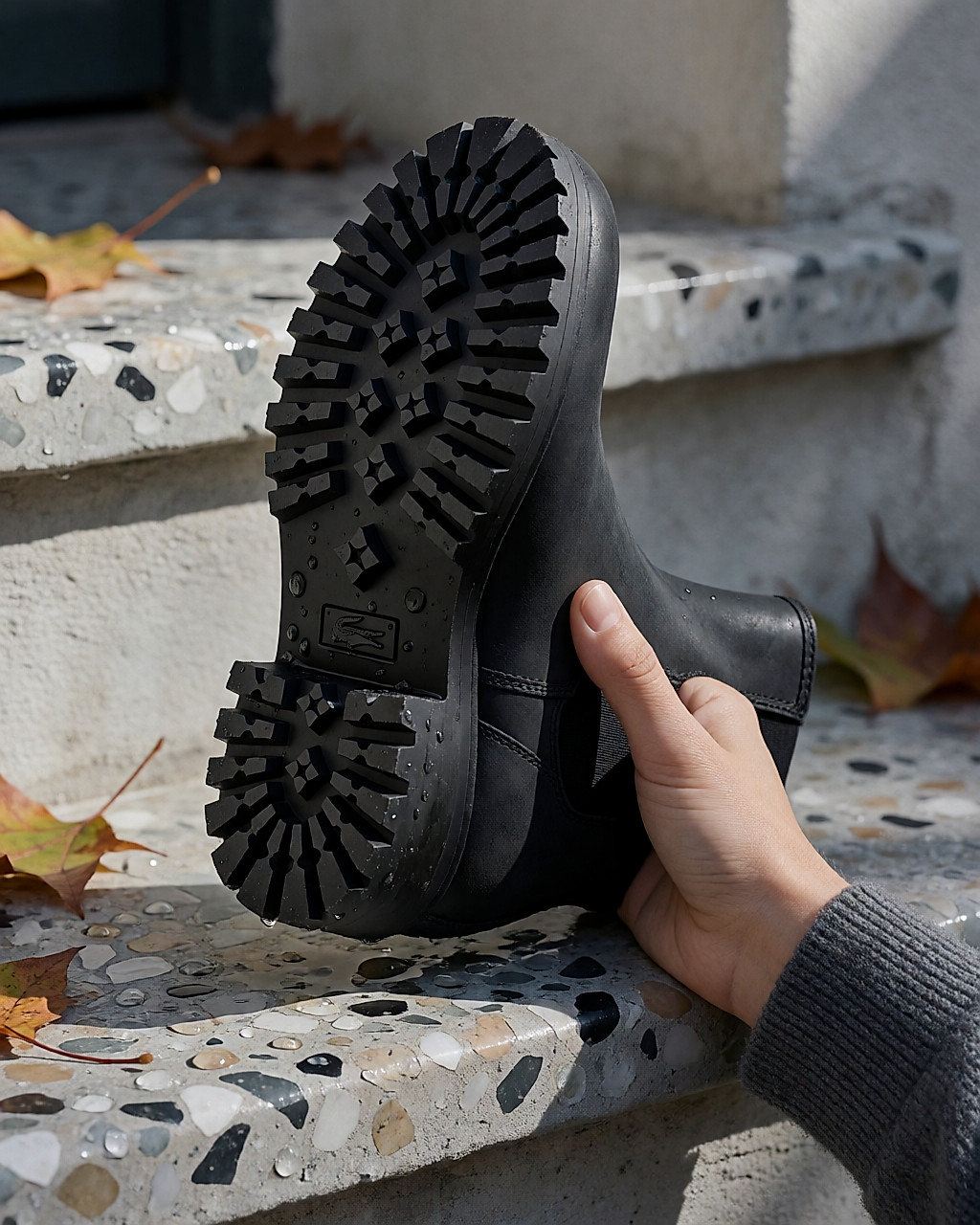 Close-up of a dense rubber lugged sole, thumb pressed into the tread of an upturned ankle boot