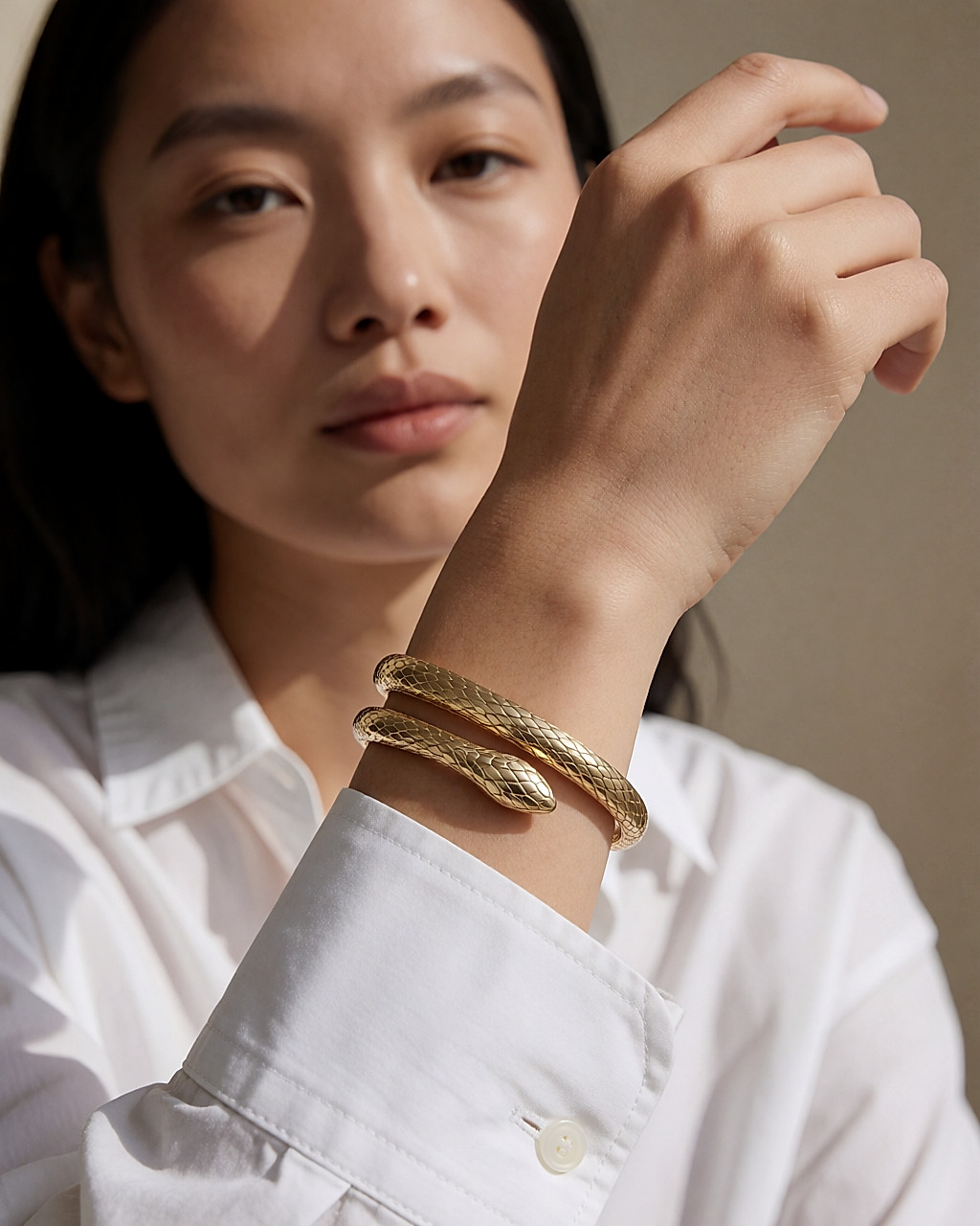 Bracelet serpent en or jaune enroulé sur un poignet sortant d'une manche de chemise