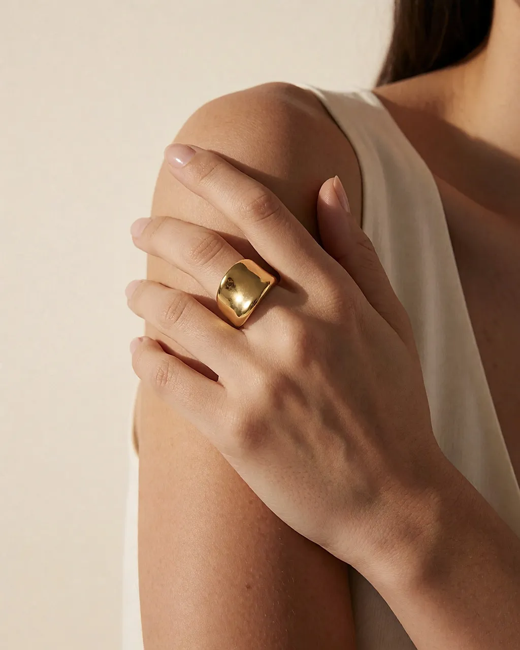 Un anillo escultural de oro llevado solo en un dedo, con muñeca y cuello libres