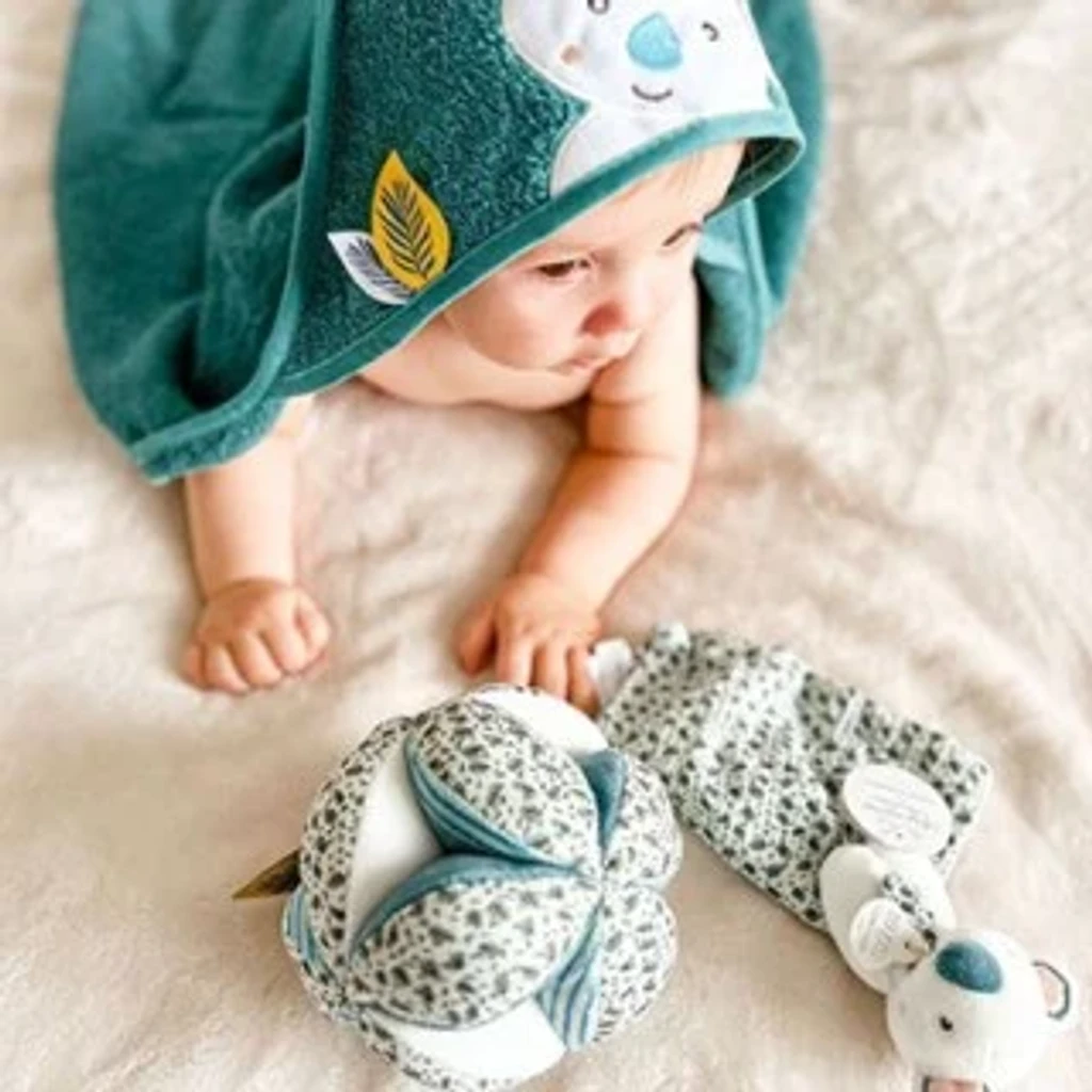 Peluche de algodón bio con las esquinas anudadas sobre una manta de lino clara, junto a un anillo de madera