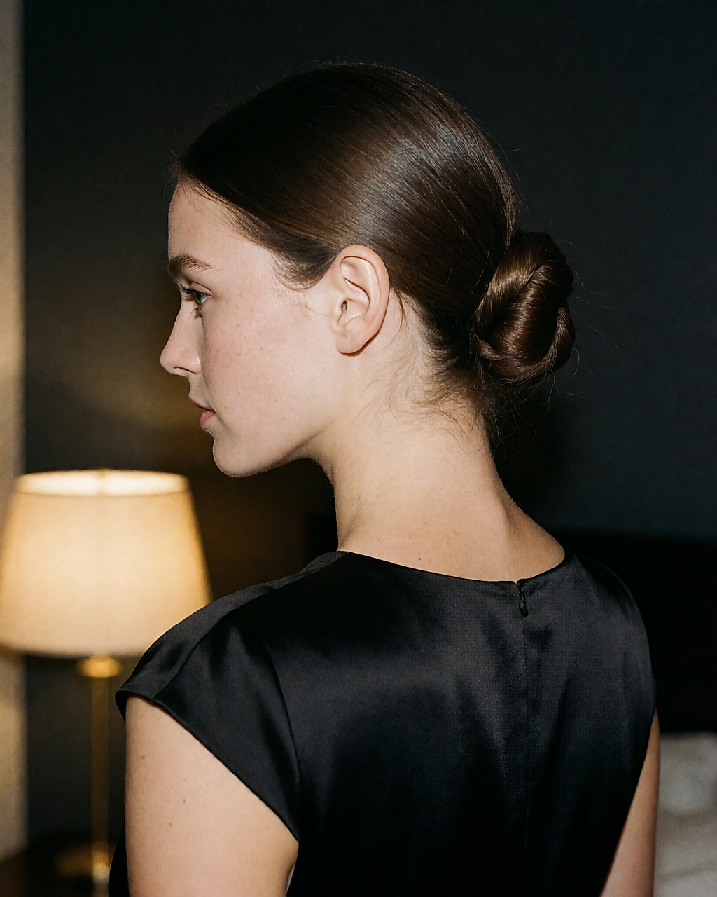 Chignon bas très lisse et brillant, enlacé d'une mèche, robe noire satinée
