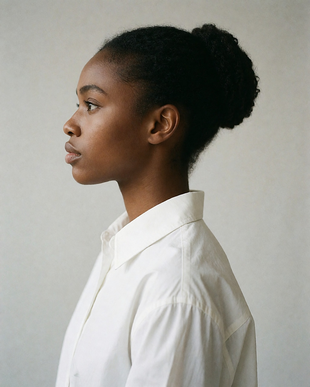 Chignon de danseuse haut sur la nuque, sans accessoire, chemise blanche à col
