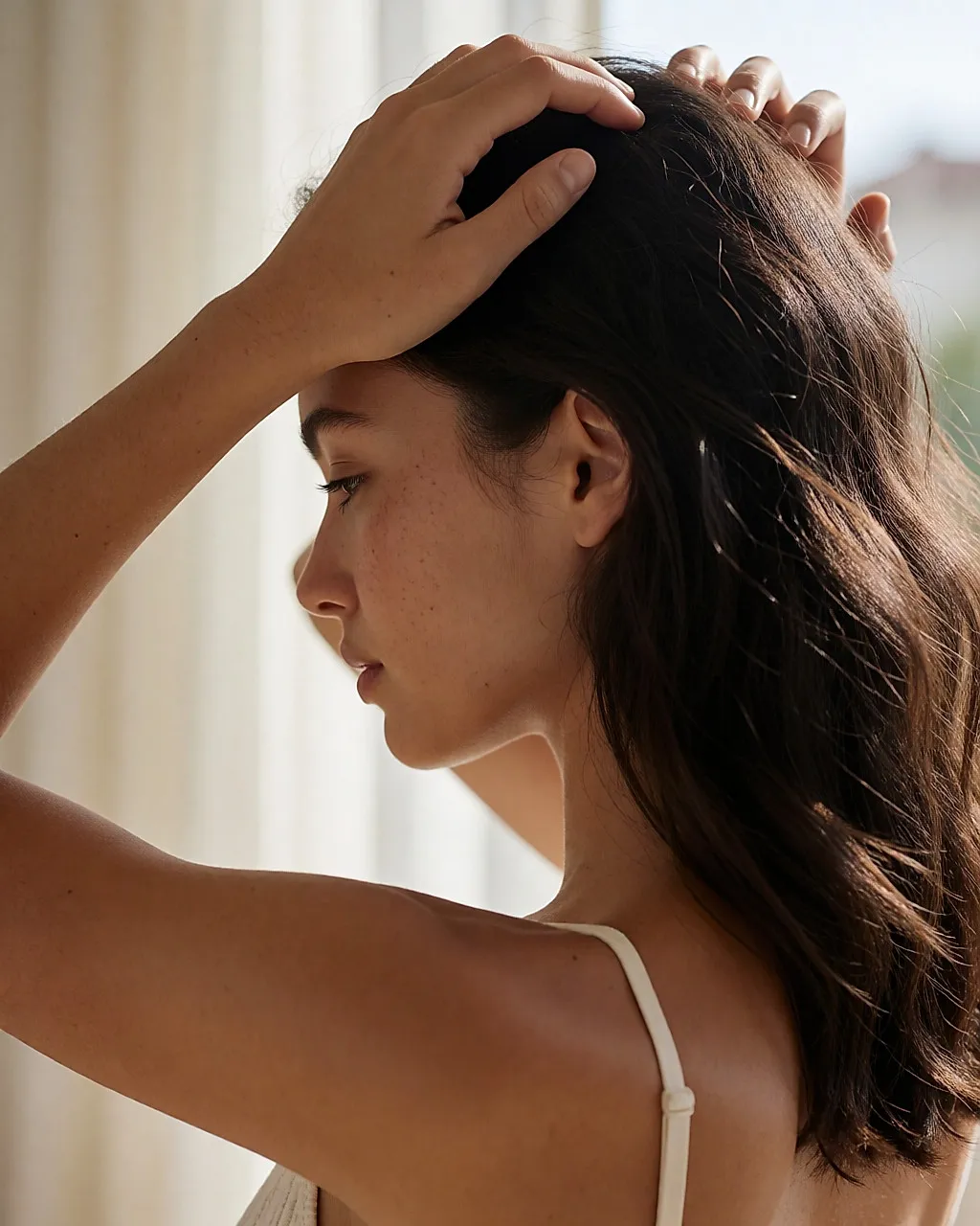 Junge Frau, die mit den Fingerspitzen ihre Kopfhaut massiert, Ansicht von schräg hinten